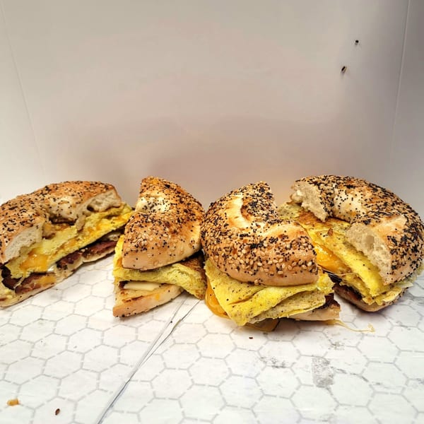 Four US Coney and Cone breakfast bagels with egg, cheese, and sausage on white paper.