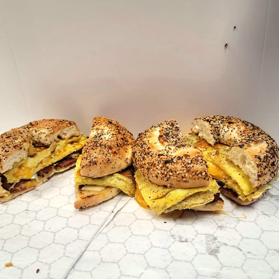 Four US Coney and Cone breakfast bagels with egg, cheese, and sausage on white paper.