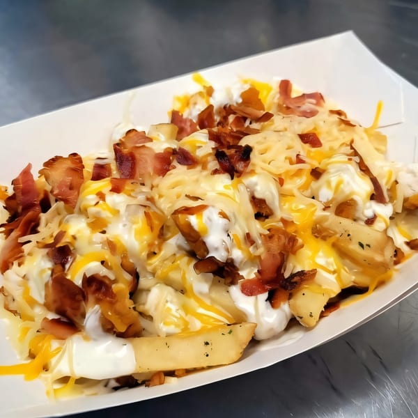 Loaded fries with melted cheese, sour cream, and crispy bacon bits in a white paper tray.