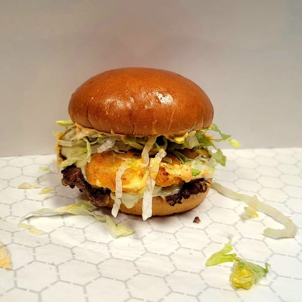 A US Coney and Cone burger with a shiny bun, lettuce, cheese, and special sauce on a patterned surface.