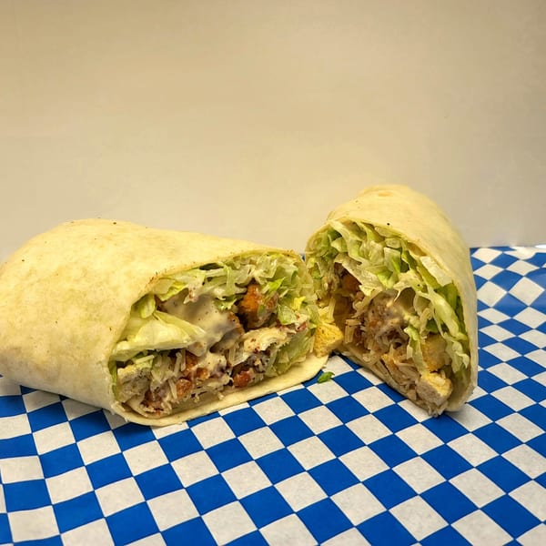 A chicken Caesar wrap, cut in half, filled with lettuce, chicken, and dressing on blue and white checkered paper.