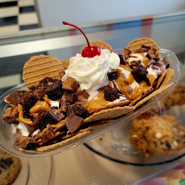 A banana split with peanut butter, chocolate, whipped cream, a cherry, and waffle cookies.