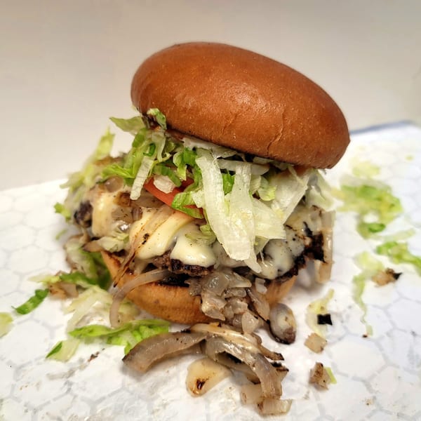 A US Coney and Cone burger with melted cheese, grilled onions, lettuce, and tomato on a bun.